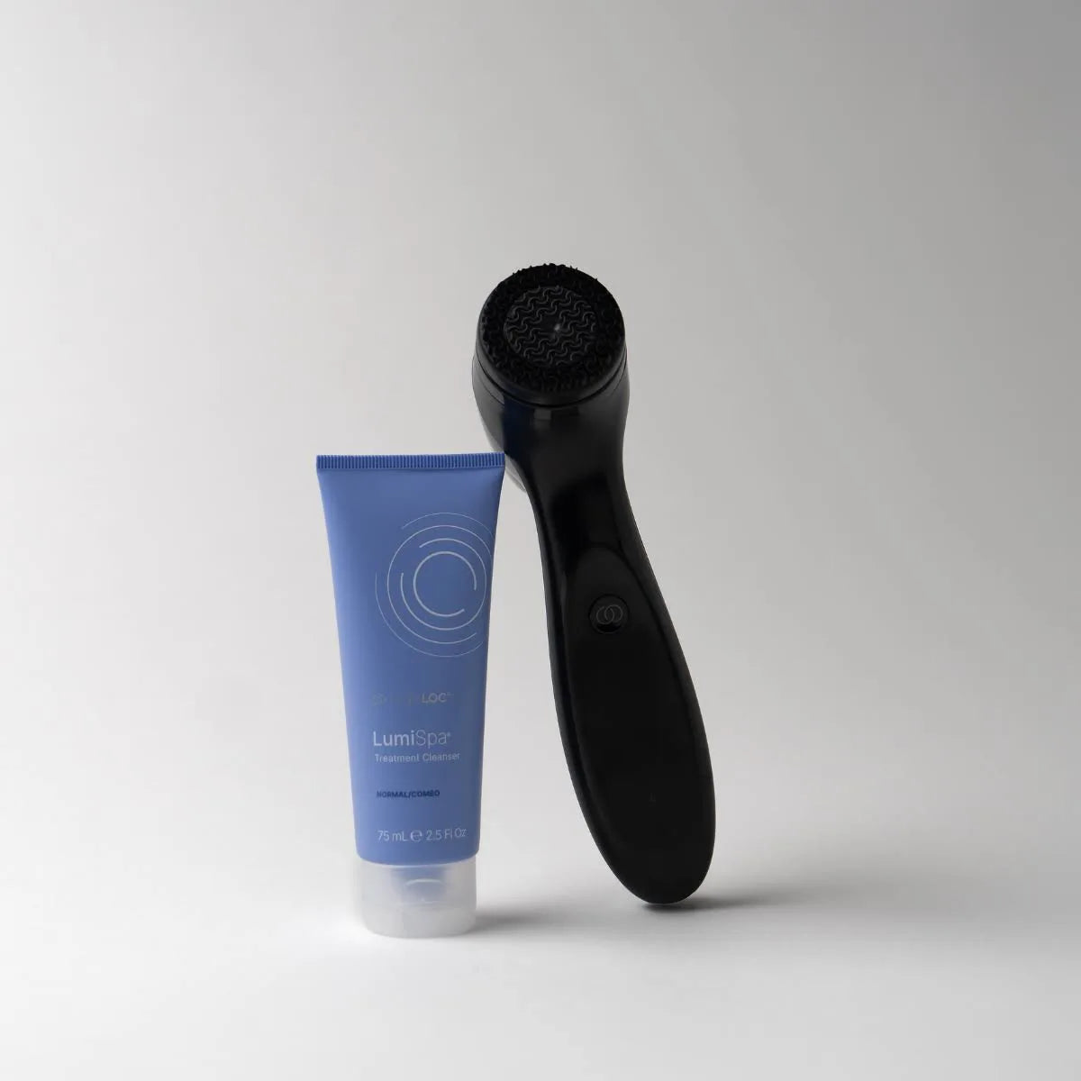 Blue tube of skincare product and black LumiSpa on a gray background