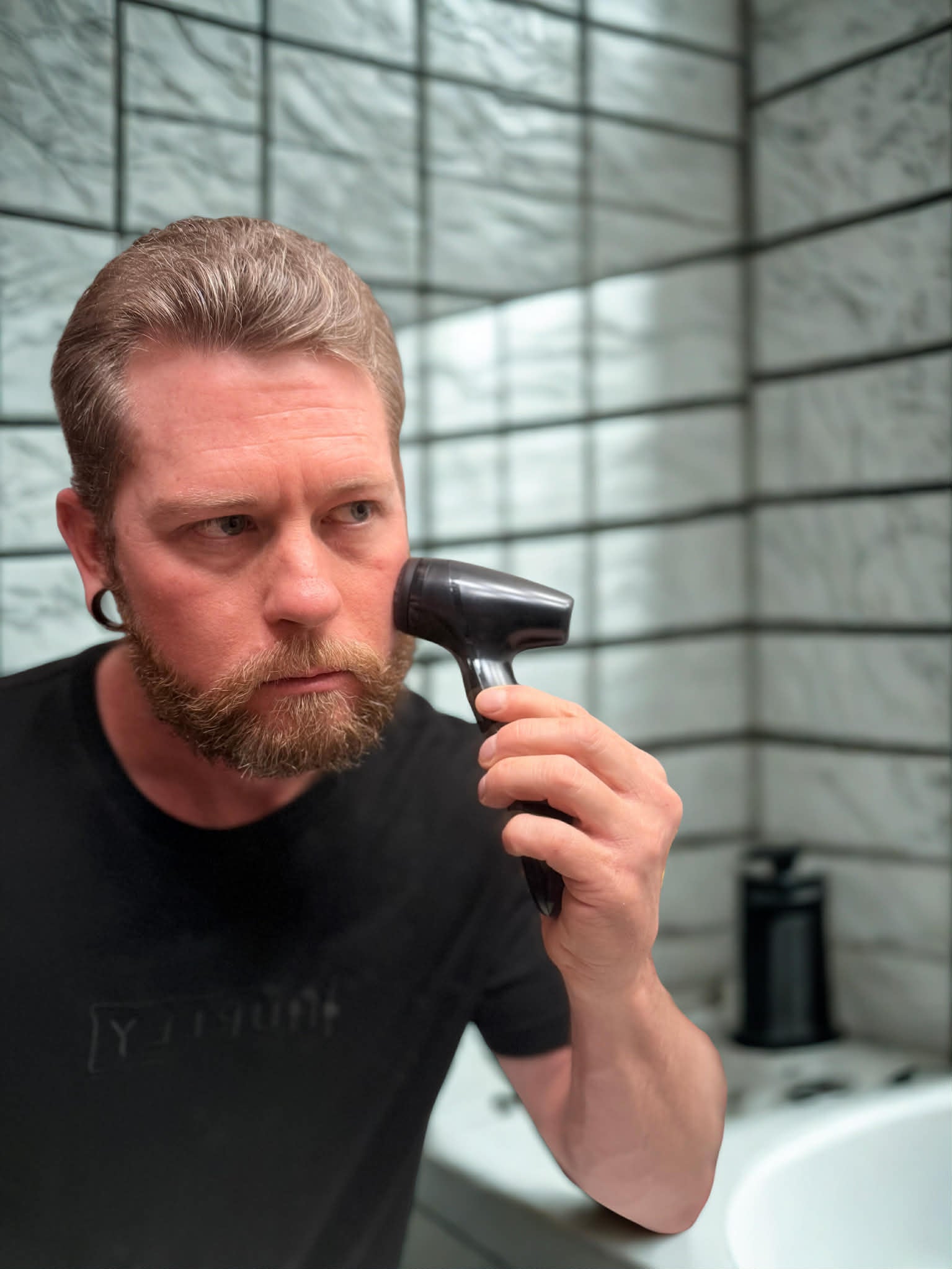 Man using a Lumispa in a bathroom with tiled walls.